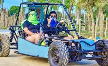 Couple enjoying a buggy ride in Punta Cana, wearing protective gear, surrounded by tropical scenery.